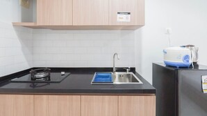 A kitchen with a black countertop, a stainless steel sink, a gas stove, and a blue and white electric kettle on a black refrigerator. - Studio Patraland Urbano Apartment (Bekasi)