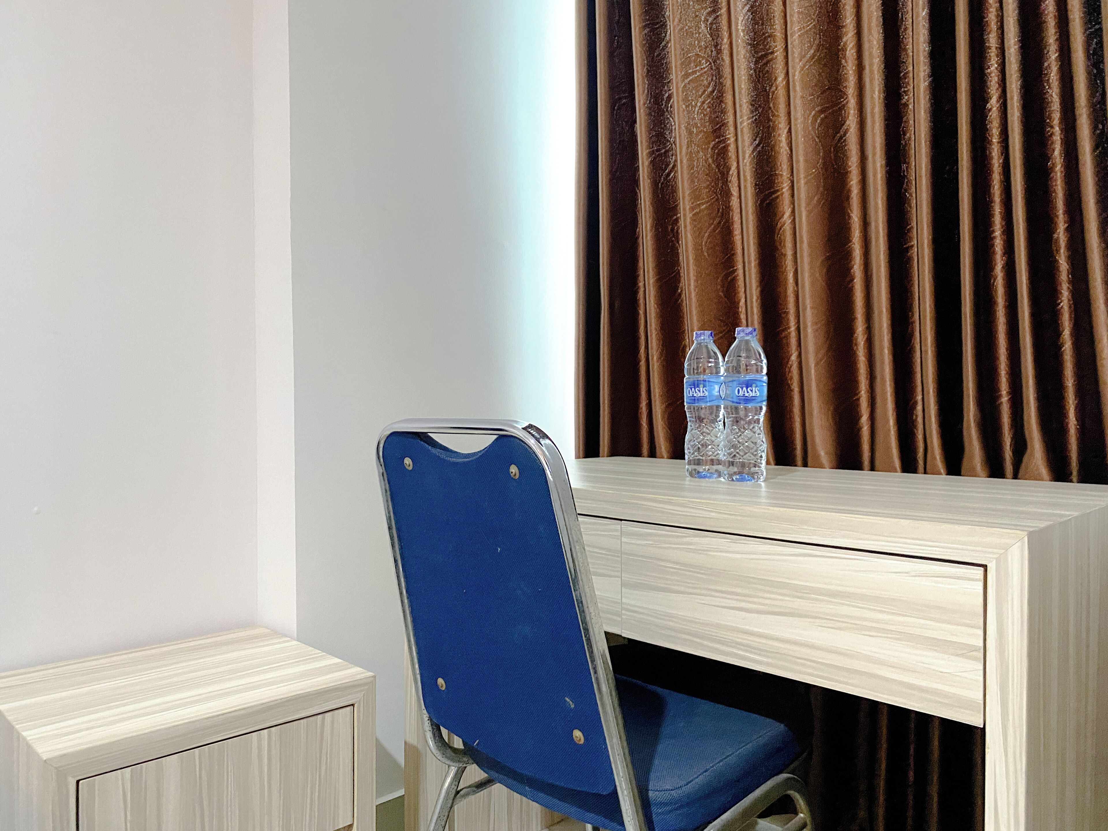 A hotel room with a wooden desk, a blue chair, and two bottles of water on the desk.