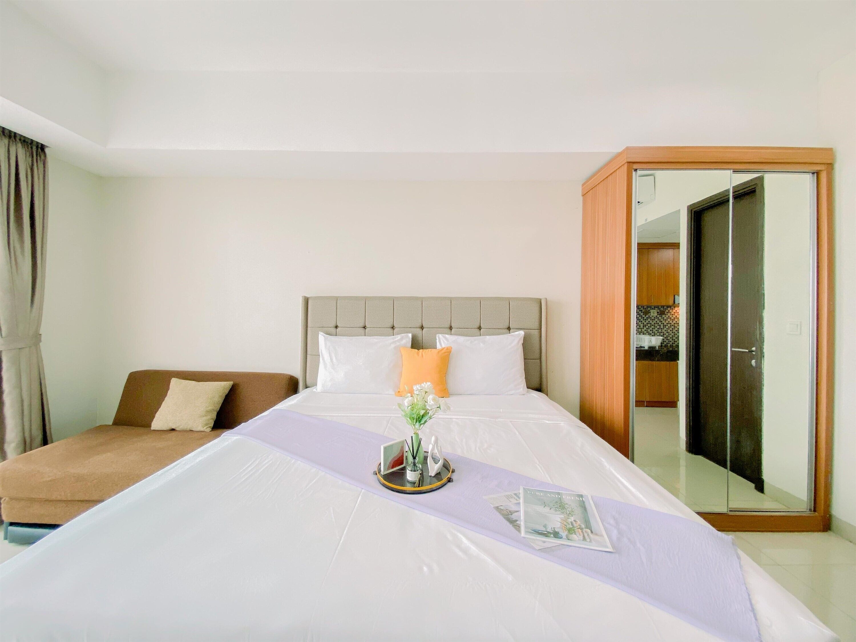 A hotel room with a bed, a sofa, a mirror, and a wardrobe.