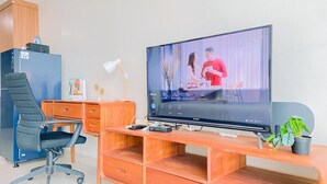 Moderni toimistoympäristö, jossa on puinen työpöytä, musta toimistotuoli, televisio ja pieni kasvi.