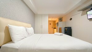 A hotel room with a bed, a nightstand, a TV, and a kitchenette. - Strategic And Homey Studio At Marquis De Lafayette Apartment (Semarang)