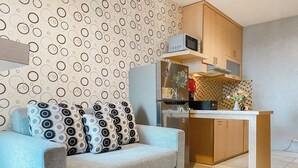 A compact living space with a sofa, a kitchen area with a microwave and a stove, and a patterned wall.