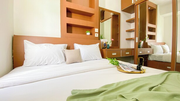 Een hotelkamer met een groot bed, een nachtkastje met een lamp, een spiegel en een kleine plant aan de muur.