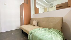 Een kleine kamer met een enkel bed, een houten garderobe, een spiegel en een groene deken op het bed.