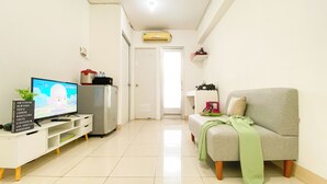 A living room with a television, a refrigerator, a sofa, and a plant. - Homey And Modern 2Br At Green Bay Pluit Apartment (Jakarta)