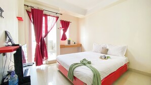 Een hotelkamer met een bed, een bureau met een computer en een raam met rode gordijnen.