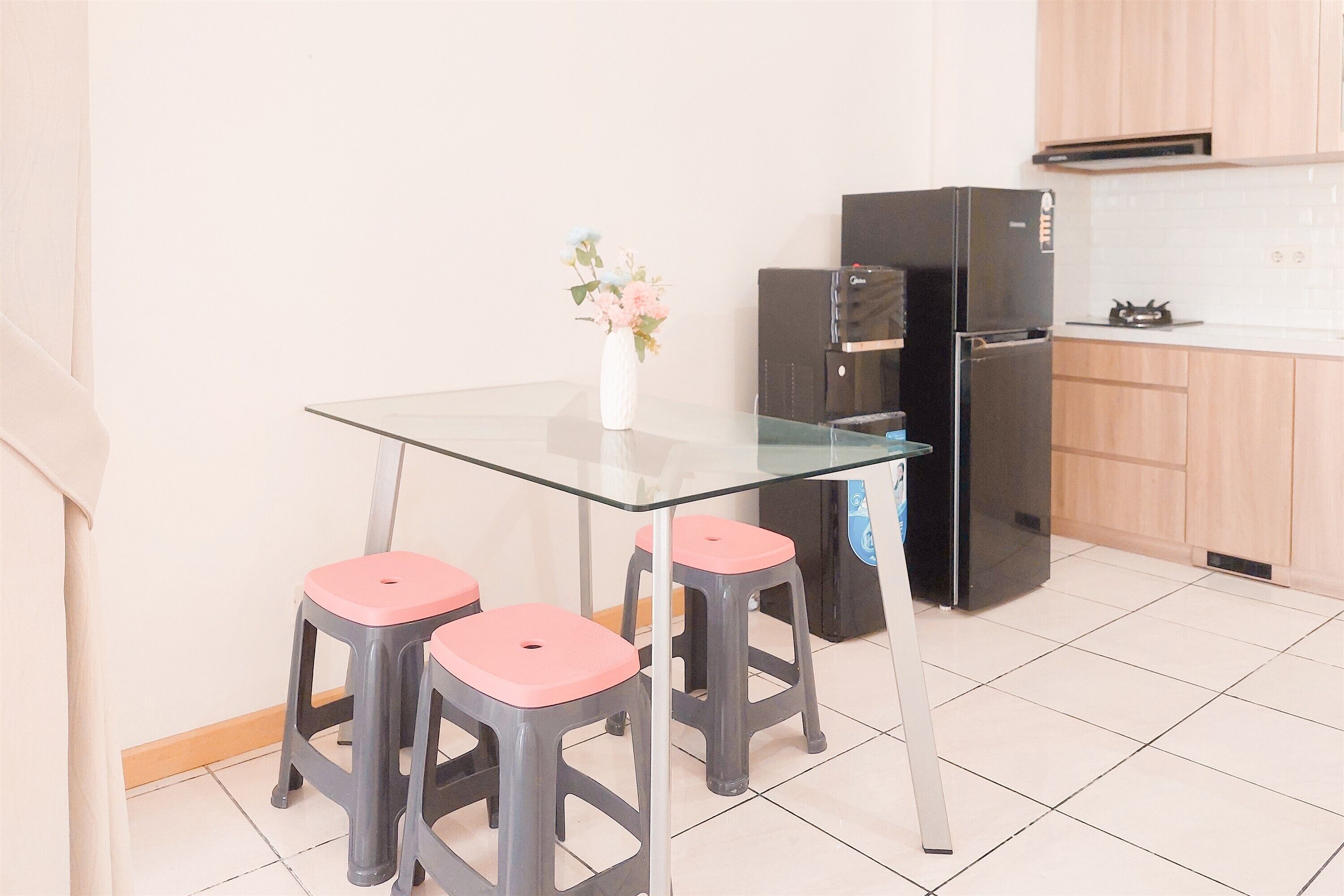 A kitchen with a glass table, three stools, a refrigerator, and a vase with flowers.