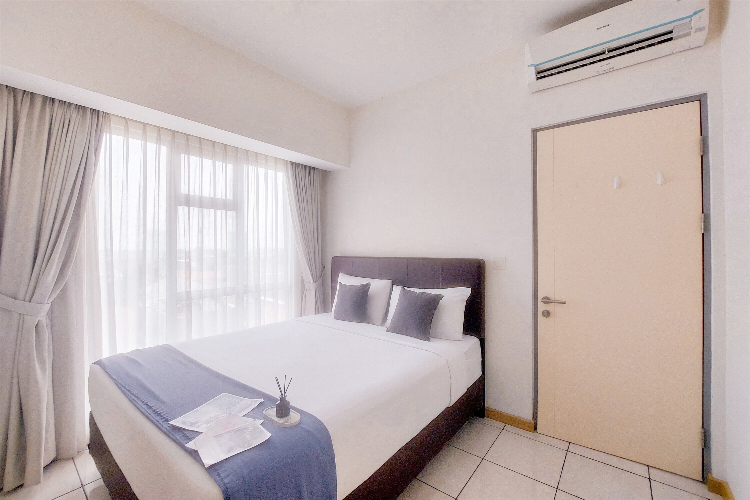 A hotel room with a bed, curtains, an air conditioning unit, and a door.