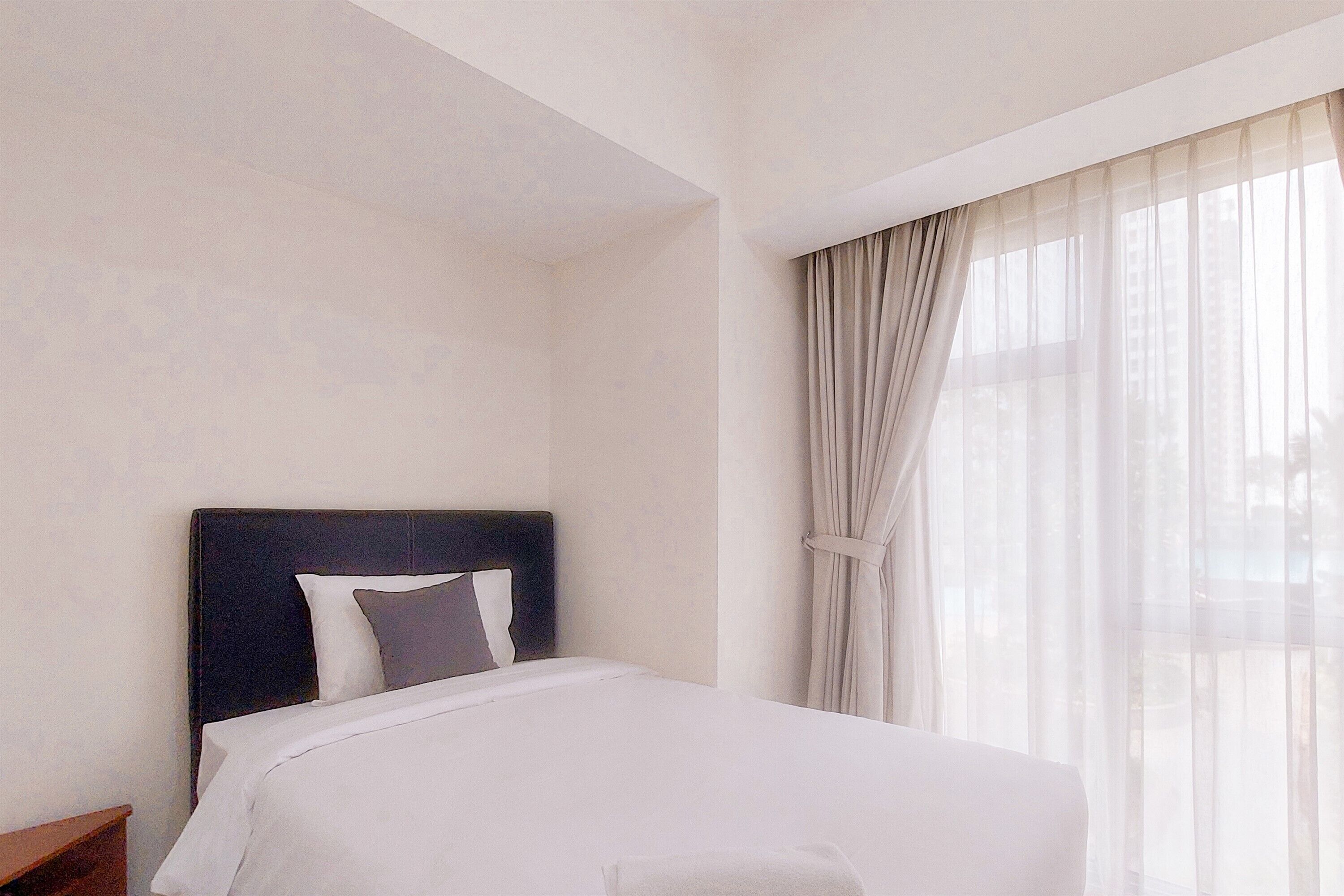 A hotel room with a bed, a nightstand, and sheer curtains on a window.