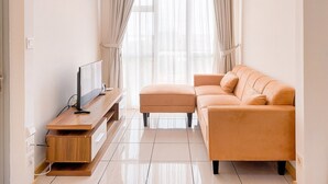 A modern living room with a sofa, ottoman, and a flat-screen TV on a wooden stand. - Comfy And Spacious 2Br Apartment M-Town Residence (Gading Serpong)