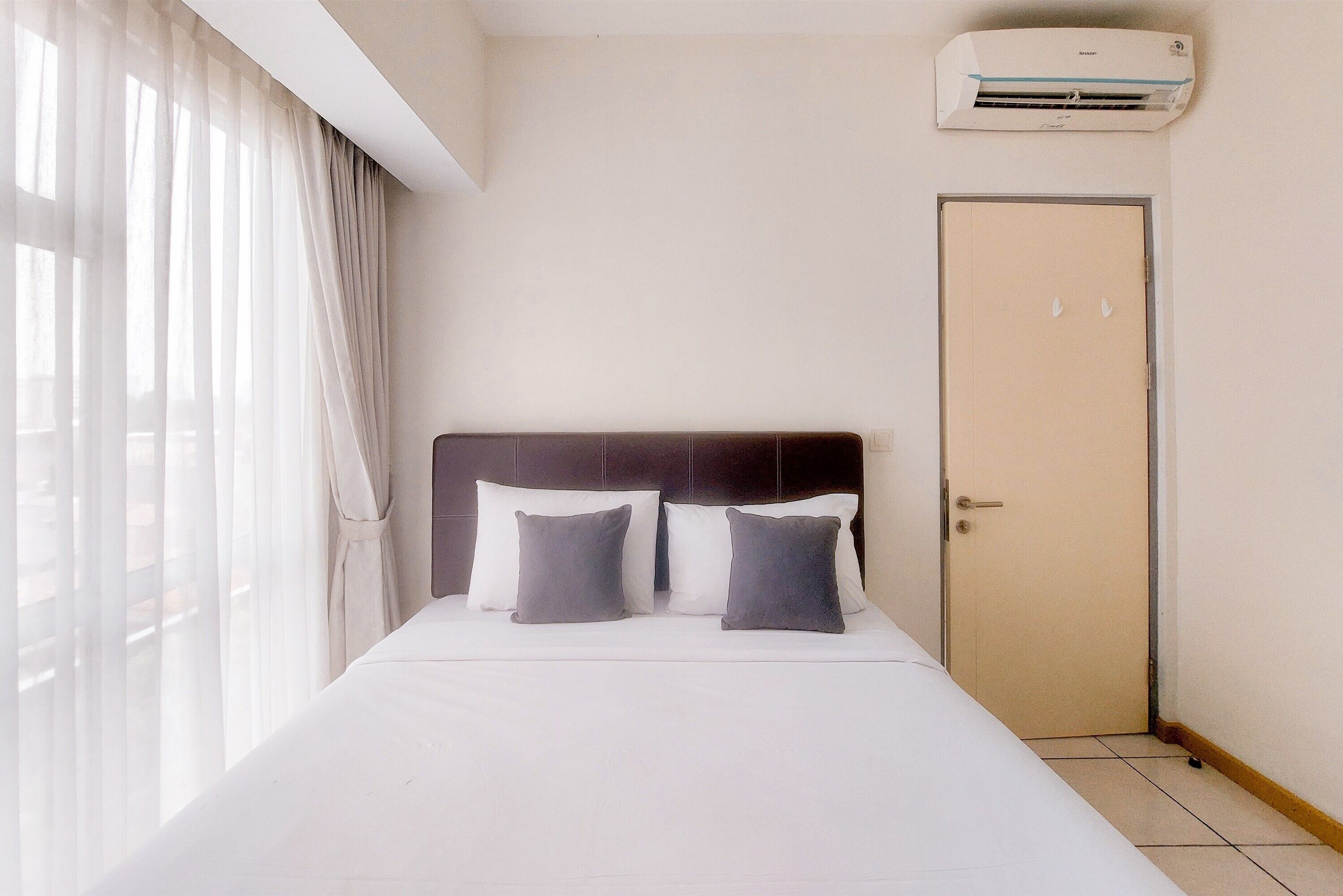 A hotel room with a bed, a door, and an air conditioning unit.