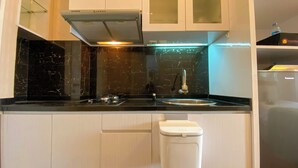 A compact kitchen with a black countertop, white cabinets, a stainless steel sink, and a trash bin.