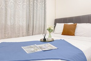 A neatly made bed with a blue bedspread, white pillows, and a brown accent pillow. A vase with white flowers and a tray with a newspaper and a pen holder are on the bed. - Good Place And Comfortable 2Br At Green Pramuka City Apartment (Jakarta)
