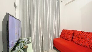 A living room with a flat-screen TV, a potted plant, a red sofa, and a curtain. - Good Place And Comfortable 2Br At Green Pramuka City Apartment (Jakarta)