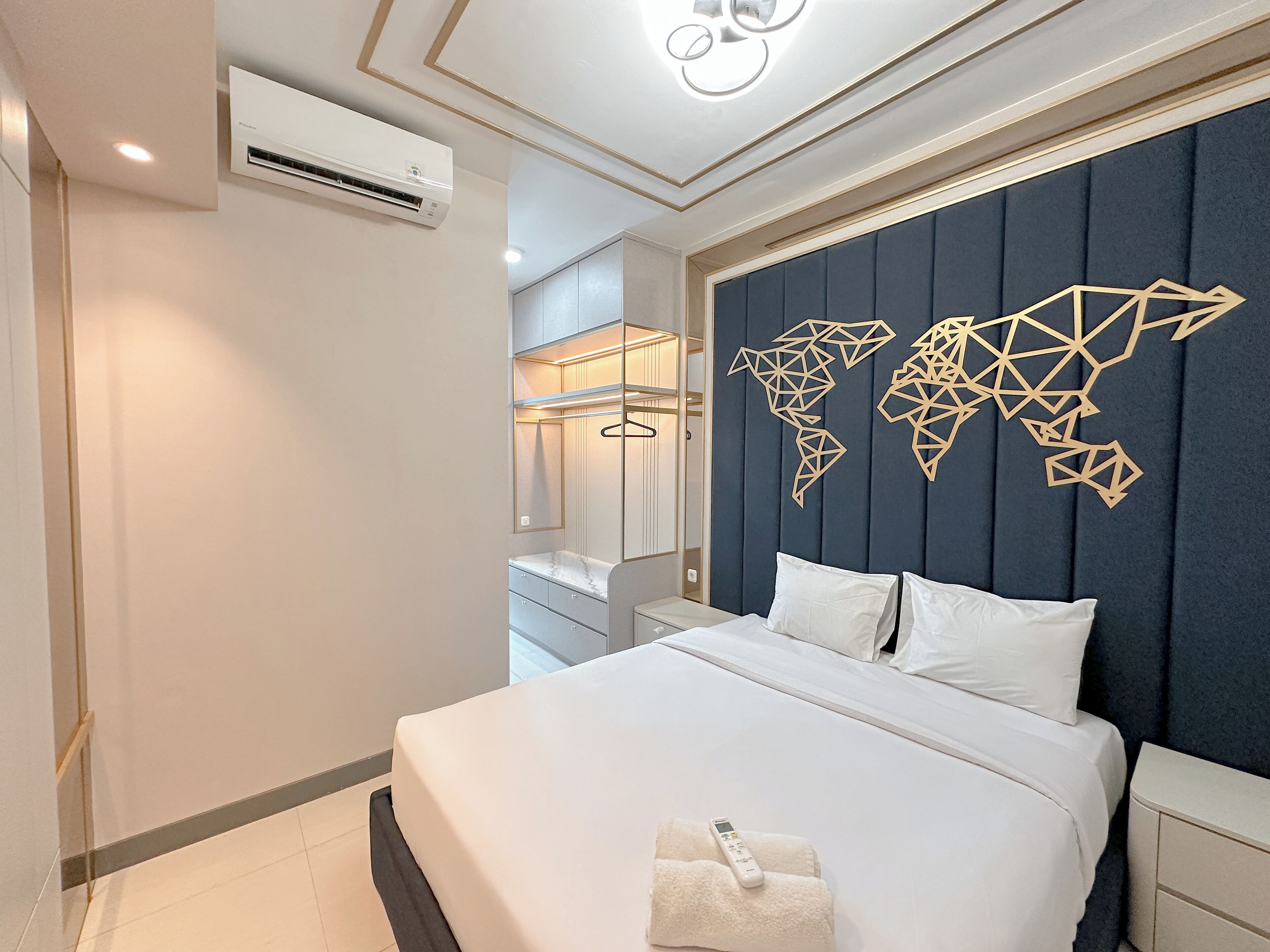 A modern hotel room with a large bed, a world map wall decoration, a wardrobe, and an air conditioning unit.