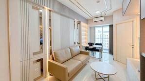 A modern living room with a beige sofa, a small round table, and a built-in bookshelf. - Great Choice And Fabulous 2Br At Benson Supermall Mansion Apartment (Surabaya)
