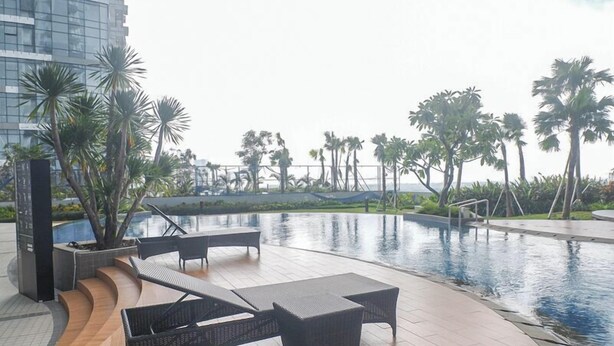A poolside area with lounge chairs and a view of palm trees and a building in the background. - Great Choice And Fabulous 2Br At Benson Supermall Mansion Apartment (Surabaya)