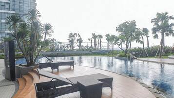 A poolside area with lounge chairs and a view of palm trees and a building in the background.