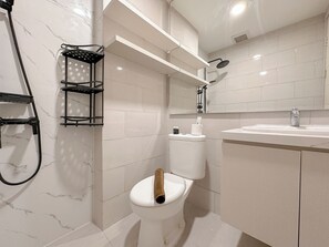 Uma casa de banho moderna com sanita, chuveiro e lavatório.
