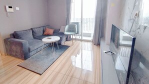 Una sala de estar moderna con un sofá gris, una mesita redonda, un televisor y un balcón con una silla.