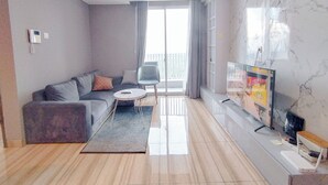 Una sala moderna con un sofá gris, una mesita redonda, un televisor y un balcón con vistas.