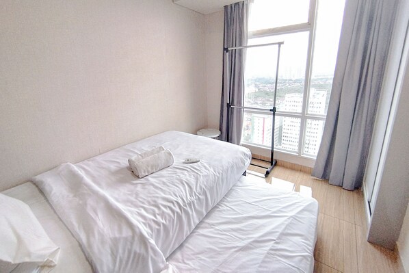 A hotel room with a bed, a window with curtains, and a view of buildings outside.