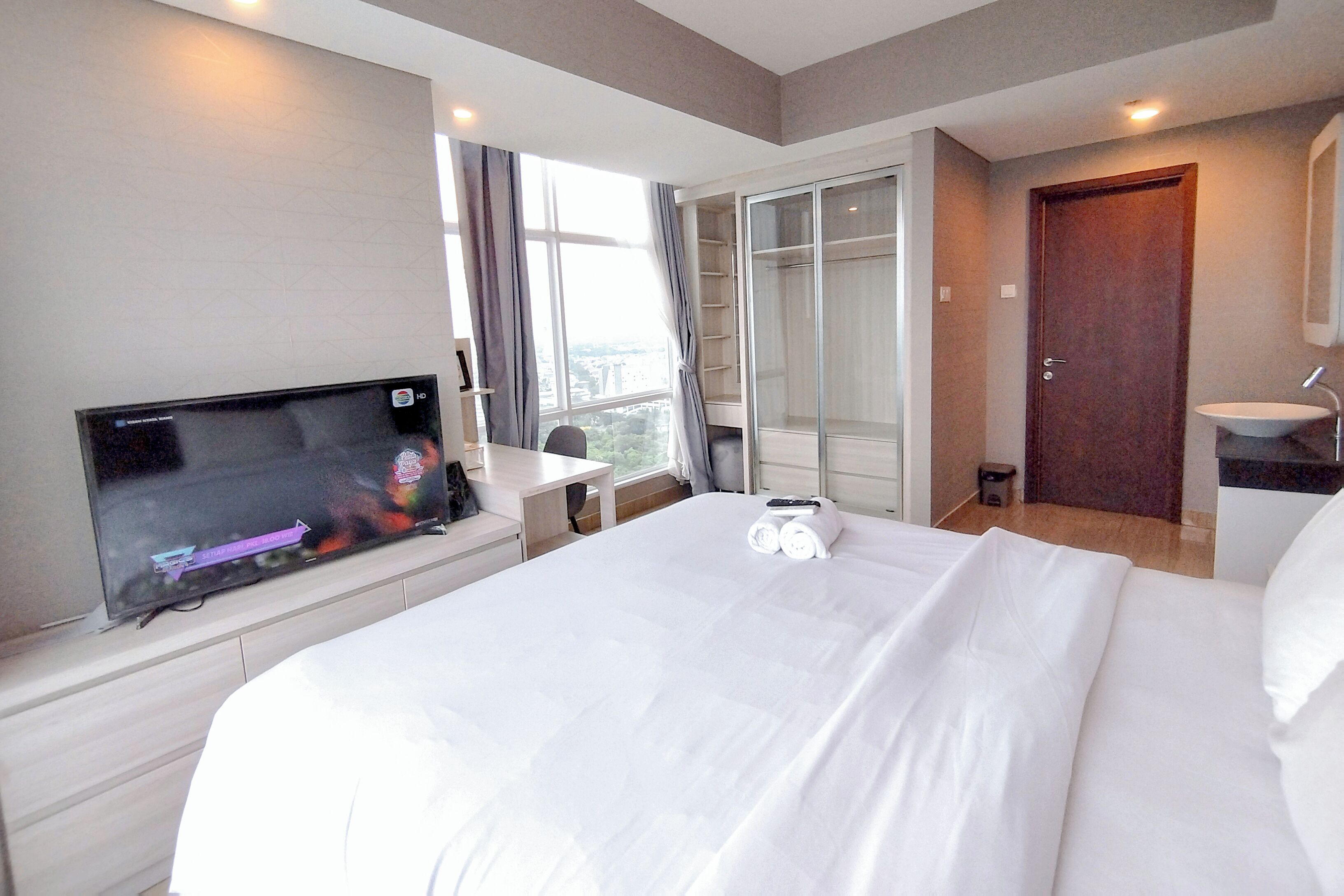 A hotel room with a large bed, a TV, a desk, a wardrobe, and a bathroom.