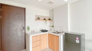 A compact kitchen with a wooden door, a built-in sink, and a refrigerator. - Cozy Studio Daan Mogot City Apartment (Jakarta)