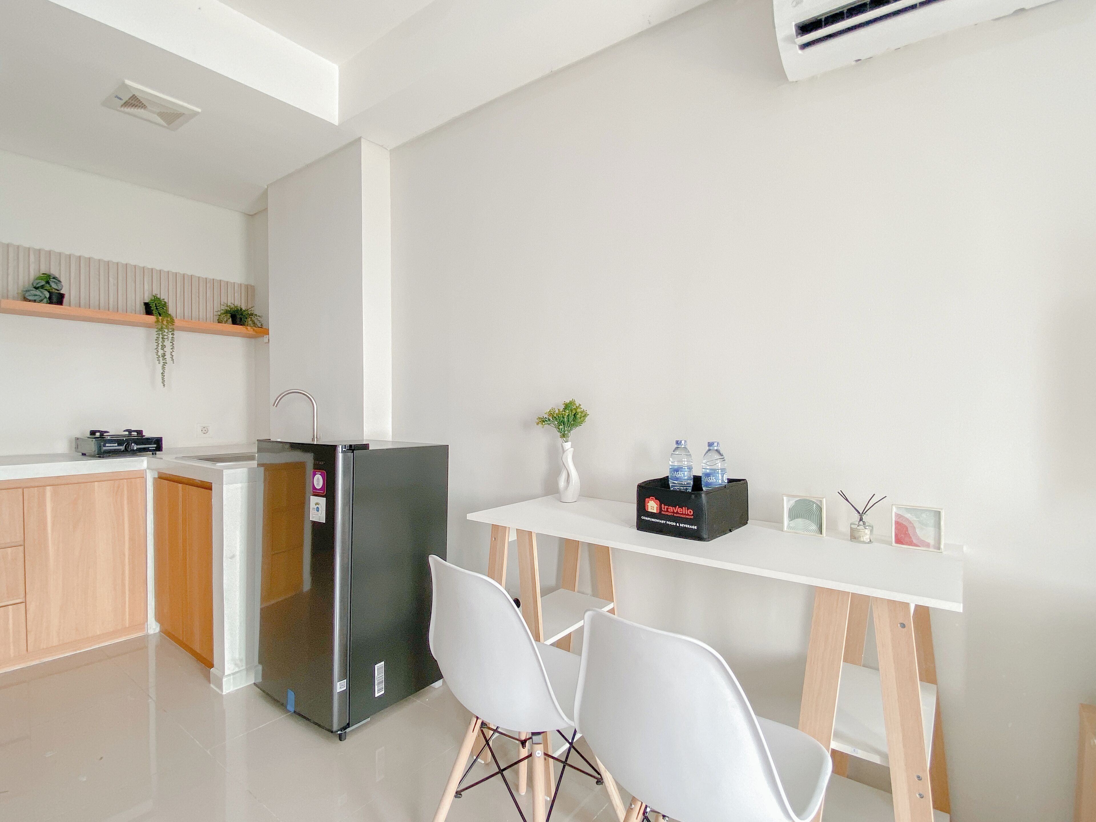 Een moderne keuken met een koelkast, een eettafel met stoelen, en een klein plankje met planten en een houder voor een waterfles.