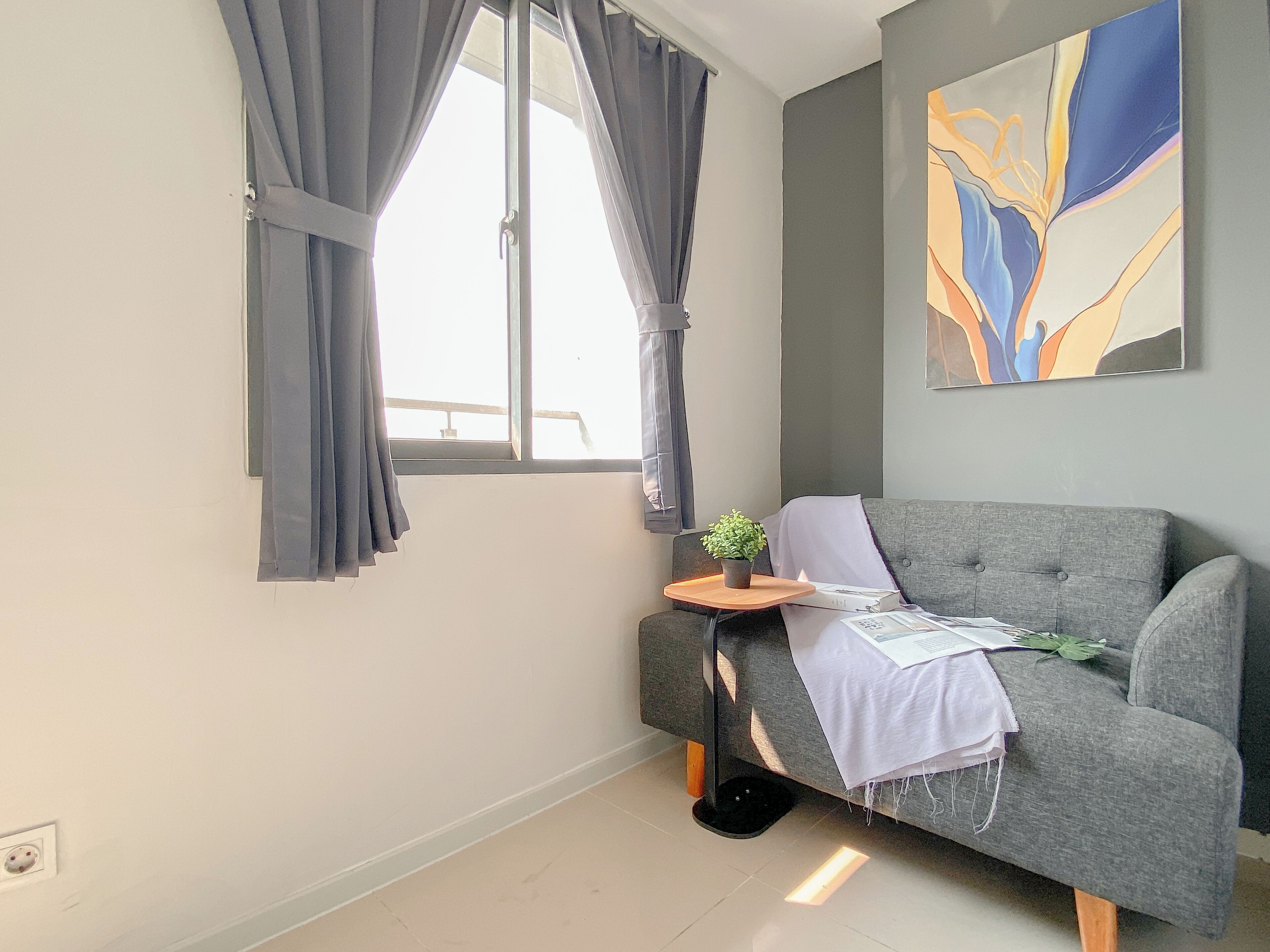 A modern living room with a grey sofa, a small side table with a plant, and a window with curtains.