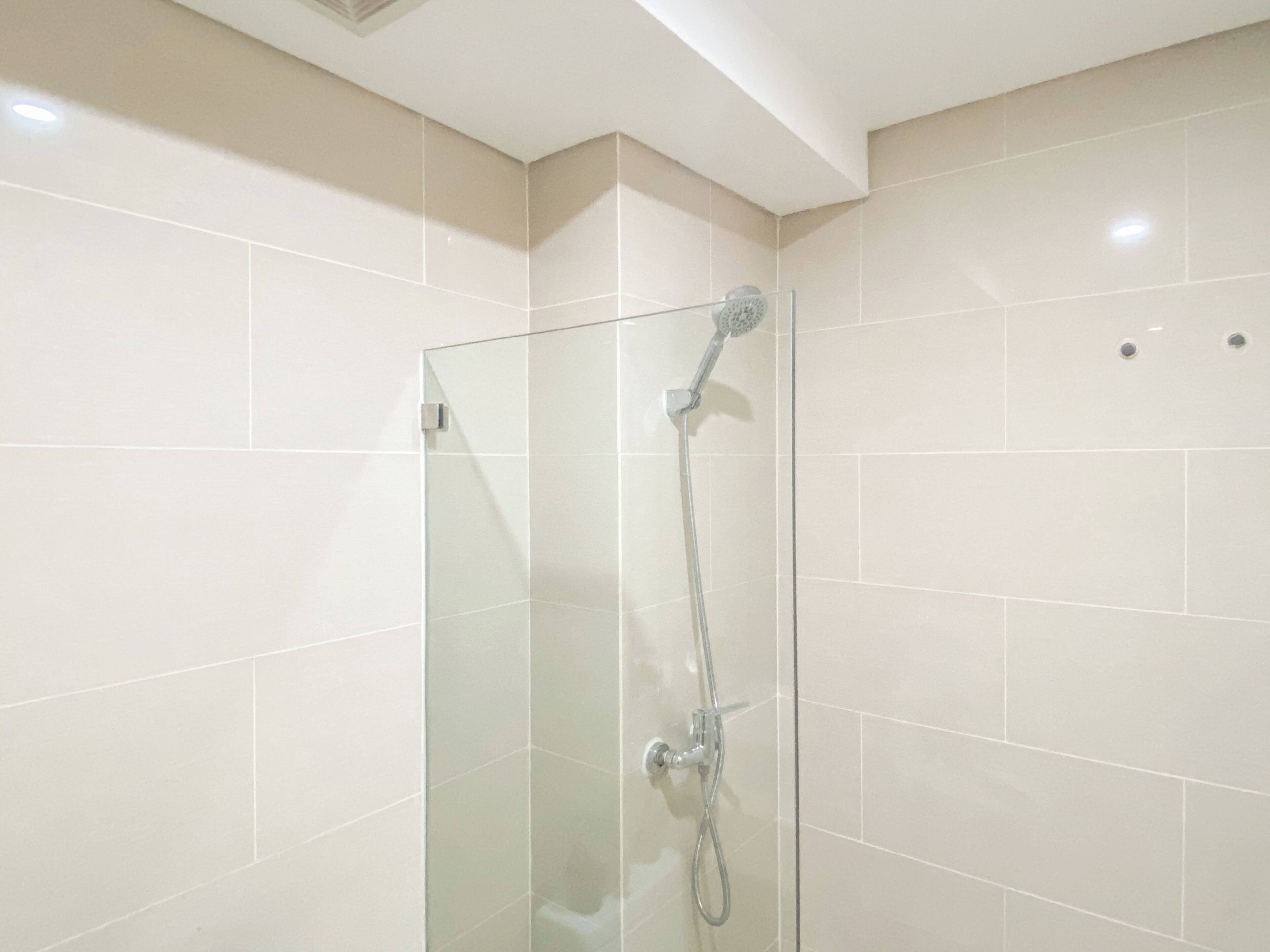 Une douche fermée par des parois en verre, dotée d’un pommeau de douche à main et d’un robinet mural.