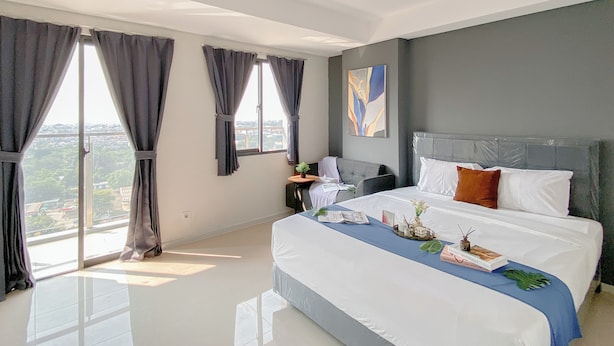 A modern bedroom with a large bed, a nightstand, and a view of the city through large windows. - Cozy Studio Daan Mogot City Apartment (Jakarta)