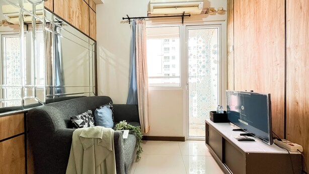 A modern living room with a sofa, a flat-screen TV, and a wooden cabinet. - Best Deal And Warm 2Br Apartment Green Pramuka City (Jakarta)