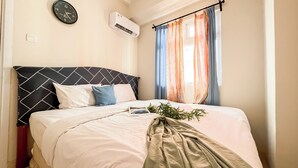 A neatly made bed with a black and white headboard, a clock, and an air conditioning unit on the wall. - Best Deal And Warm 2Br Apartment Green Pramuka City (Jakarta)