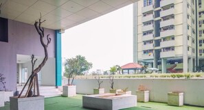 An outdoor area with artificial turf, concrete planters, and a building with balconies in the background. - Minimalist And Homey Studio Apartment Amethyst (Jakarta)