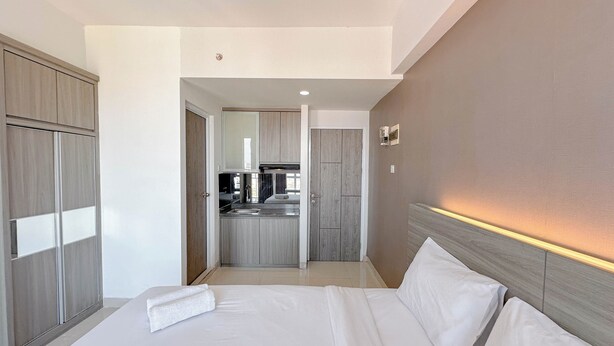 A hotel room with a bed, a wardrobe, and a kitchenette in the background. - Good Deal Stunning Studio (No Kitchen) At Taman Melati Surabaya Apartment (Surabaya)