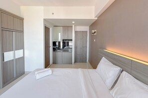 A hotel room with a bed, a wardrobe, and a kitchenette in the background. - Good Deal Stunning Studio (No Kitchen) At Taman Melati Surabaya Apartment (Surabaya)