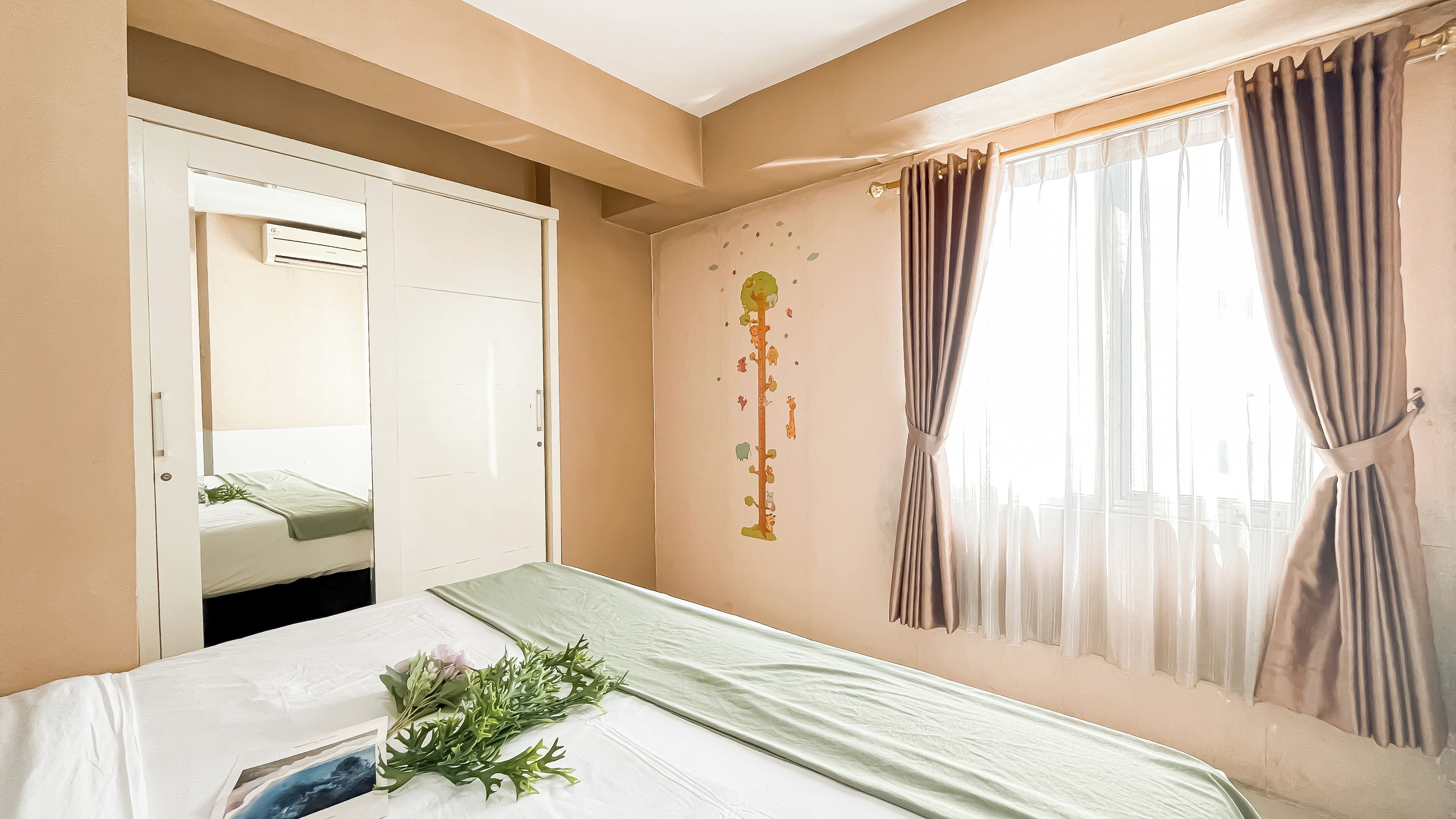 Una habitación de hotel con cama, ventana con cortinas, decoración en la pared y equipo de aire acondicionado.
