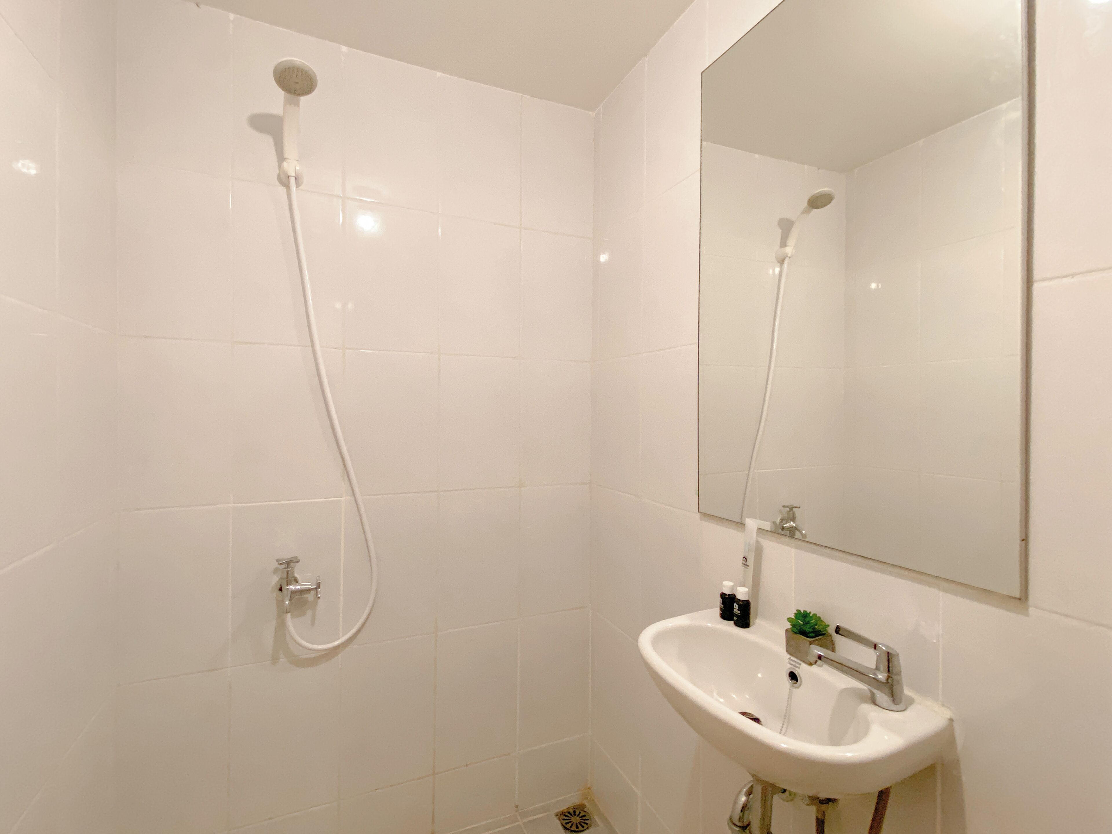 A bathroom with white tiles, a sink, a mirror, and a shower.