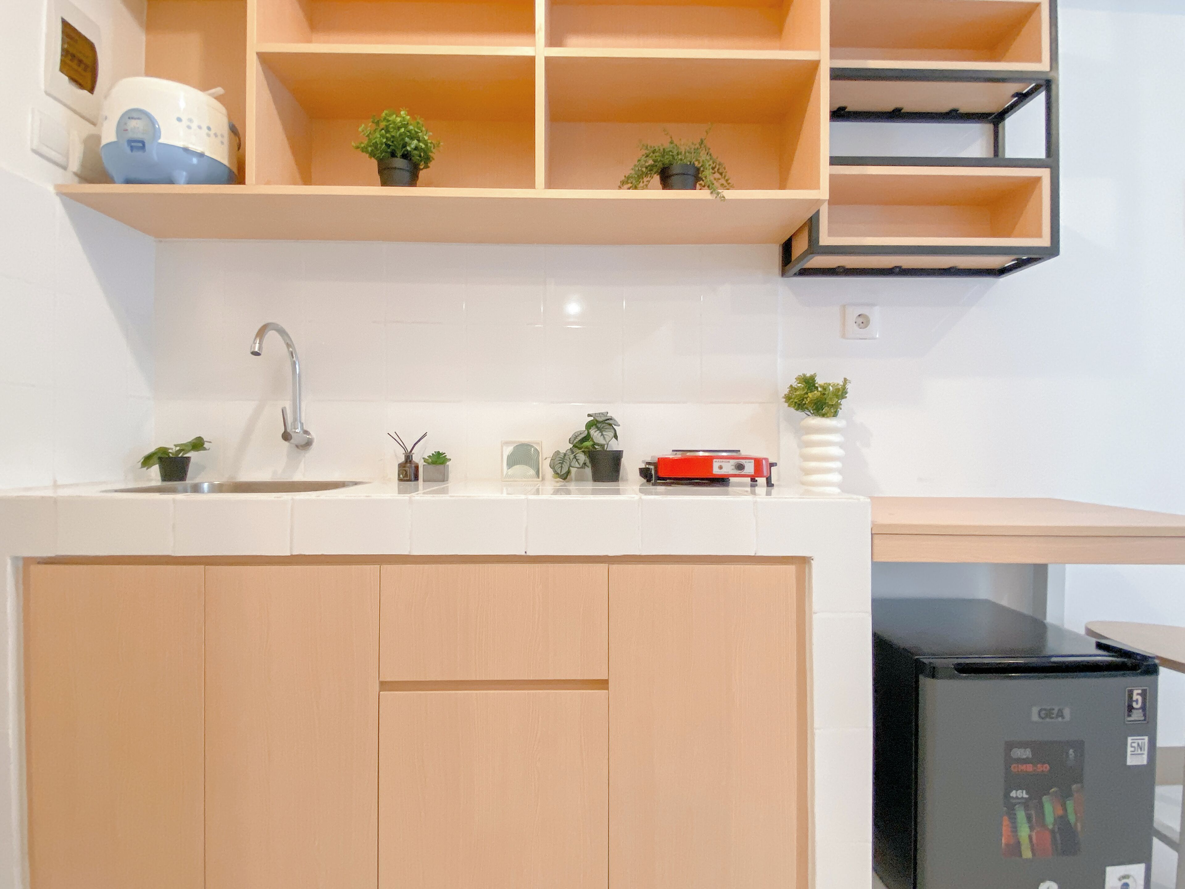 Una cocina con pileta, mostrador y armarios de madera. Hay plantas en macetas sobre el mostrador y un electrodoméstico negro a la derecha.
