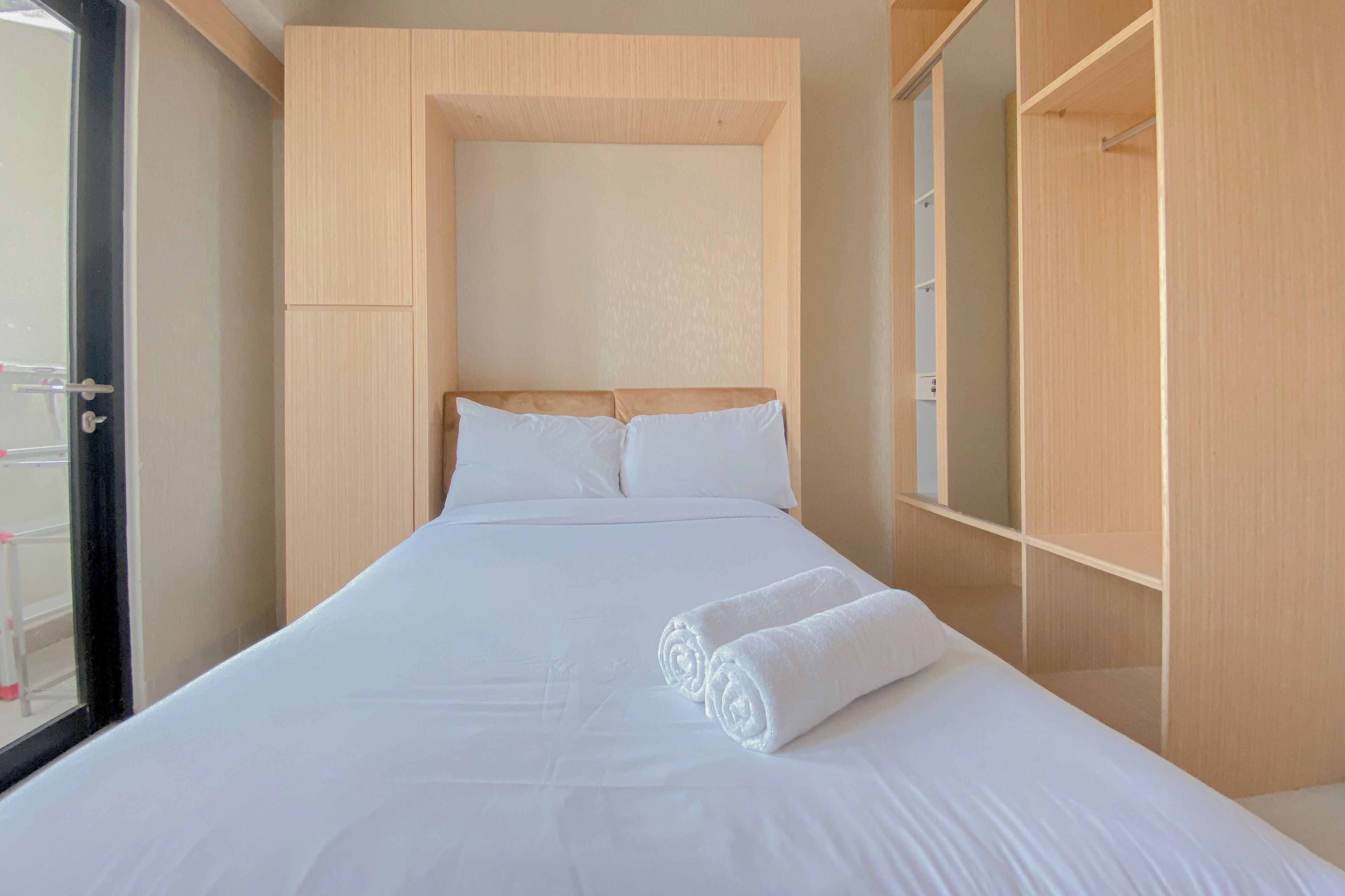 A neatly made bed with white linens and two rolled towels, a wooden wardrobe, and a glass door leading to a balcony.