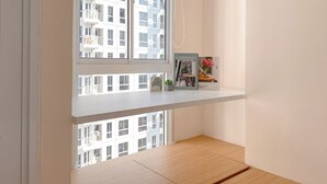 A room with a wooden floor, a white wall, and a window overlooking a building. - Enjoy Living Studio At Tokyo Riverside Pik 2 Apartment (Teluknaga)
