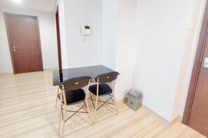 A small room with a wooden floor, a black table, two chairs, a trash bin, and a door. - 2Br Minimalist And Simply At Grand Sungkono Lagoon Apartment (Surabaya)