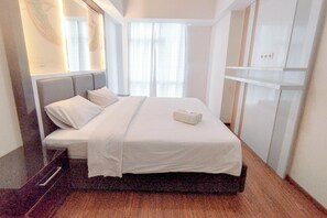 A modern hotel room with a neatly made bed, a built-in wardrobe, and a large window with sheer curtains. - 2Br Minimalist And Simply At Grand Sungkono Lagoon Apartment (Surabaya)