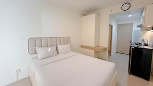 Une chambre d’hôtel moderne avec un grand lit, une armoire intégrée, une petite kitchenette et une horloge murale.