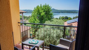 A balcony with wicker furniture, a table with a tray, and a view of a lake and hills. - Cozy House with Lake View • Private Terrace & Self Check-in 24h (Viverone)