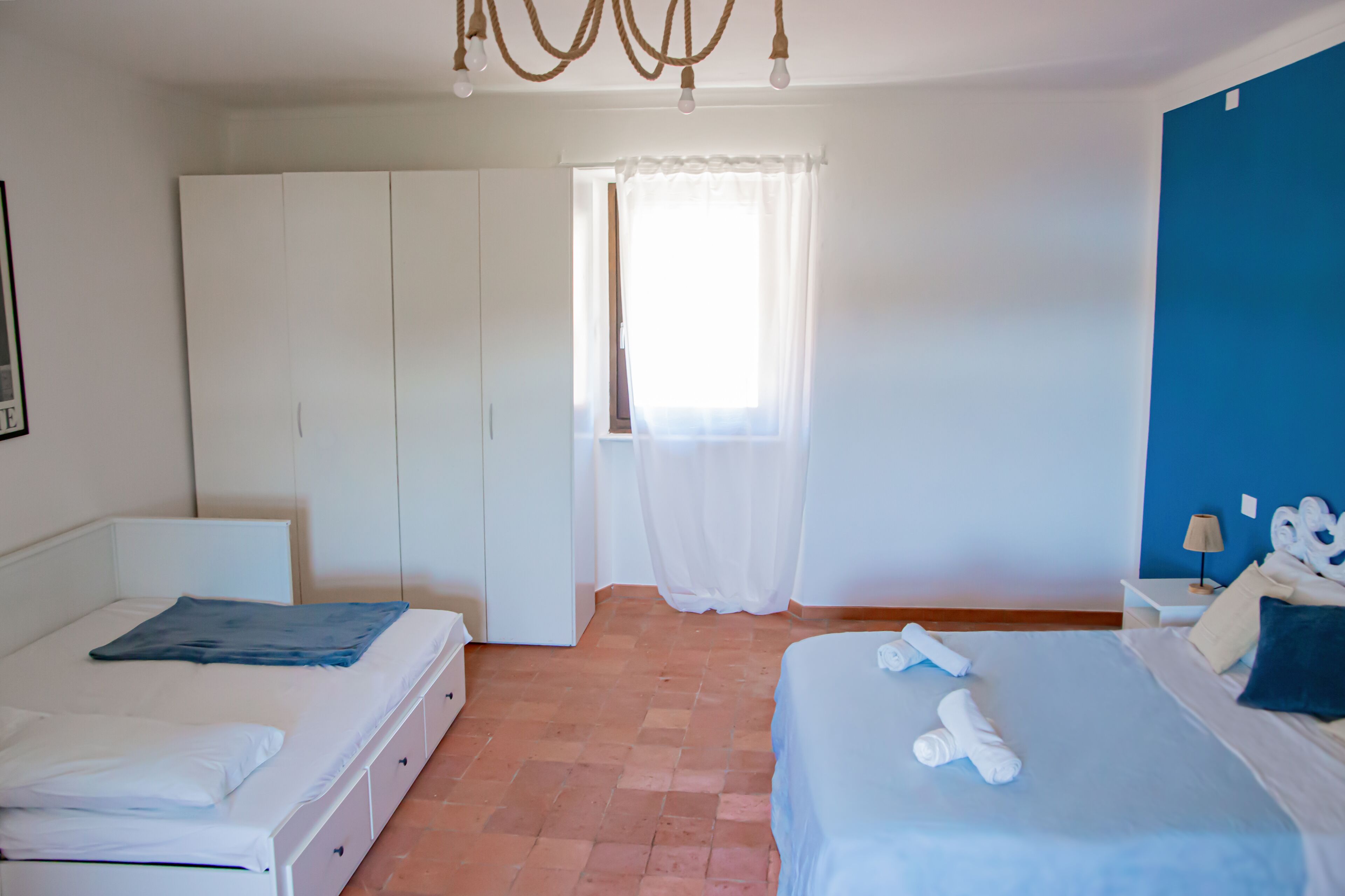A bedroom with a bed, a wardrobe, a window with curtains, and a blue wall.