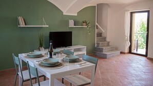 A dining area with a table set for four, a television, and a staircase leading to a balcony. - Cozy House with Lake View • Private Terrace & Self Check-in 24h (Viverone)