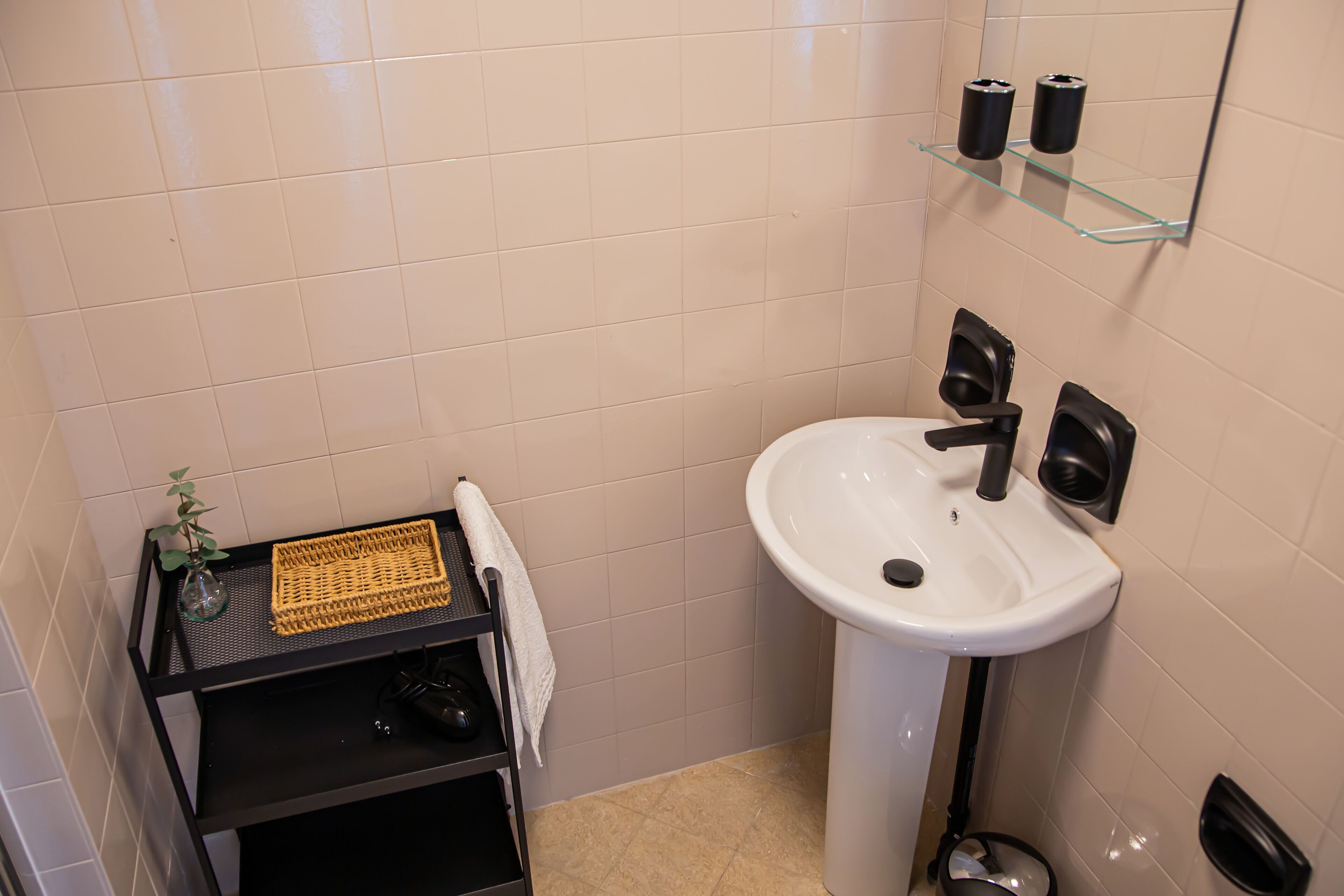 Ein Badezimmer mit einem weißen Waschbecken, einem schwarzen Handtuchhalter und einem Glastablett mit Toilettenartikeln.
