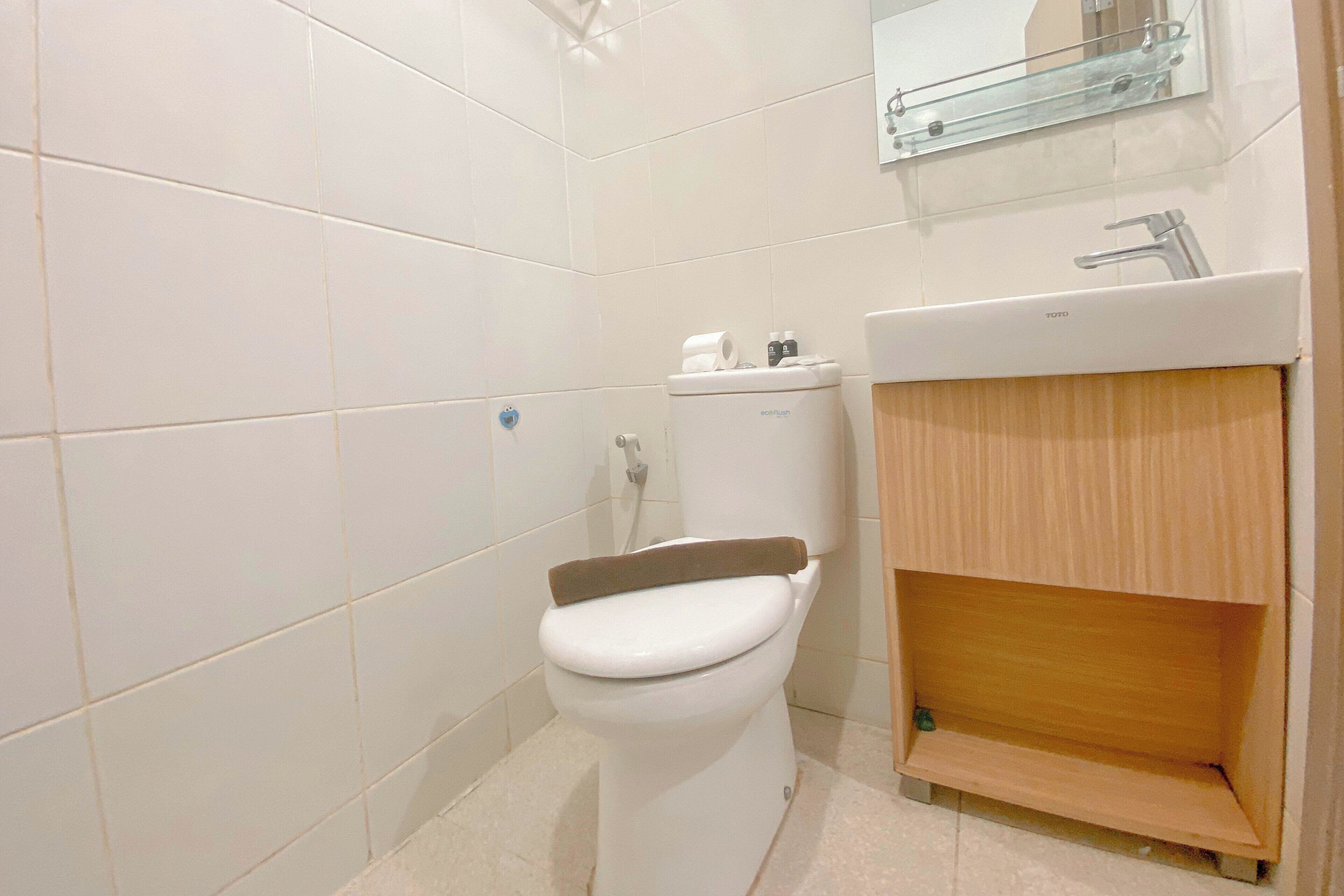 A small, clean bathroom with white tiles, a toilet, a sink, and a mirror above the sink.